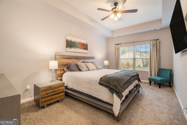 carpeted bedroom with ceiling fan and a raised ceiling