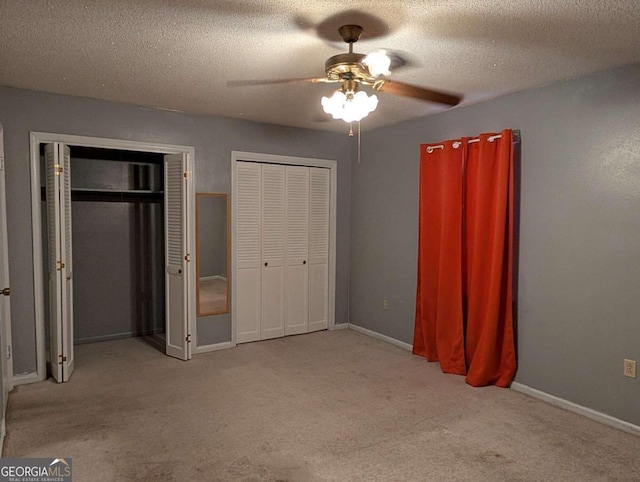 unfurnished bedroom featuring a textured ceiling, light colored carpet, ceiling fan, and multiple closets