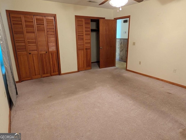 unfurnished bedroom featuring light carpet, ceiling fan, and multiple closets