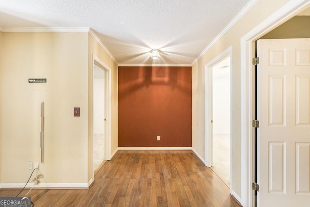 hallway featuring a textured ceiling, ornamental molding, wood finished floors, and baseboards