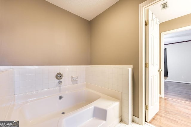 full bathroom featuring wood finished floors, visible vents, baseboards, and a bath