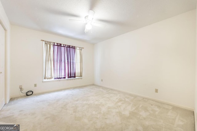 empty room with light carpet, ceiling fan, a textured ceiling, and baseboards