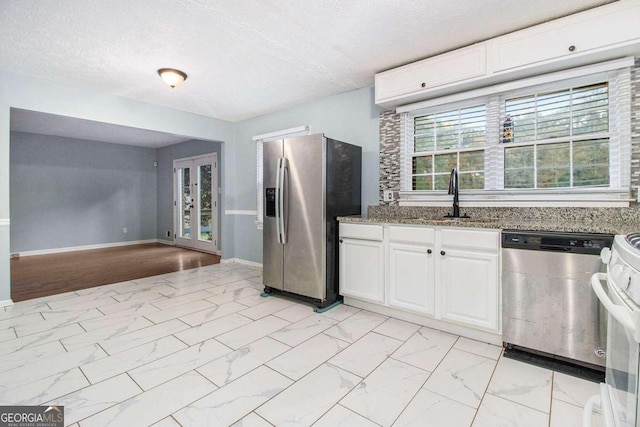 kitchen with appliances with stainless steel finishes, dark stone counters, a textured ceiling, sink, and white cabinetry