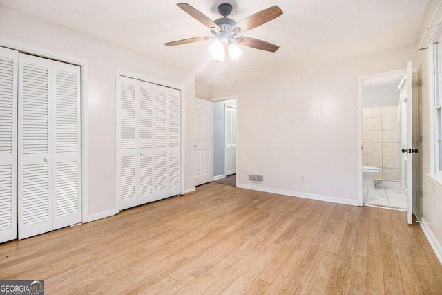 unfurnished bedroom featuring multiple closets, ensuite bathroom, ceiling fan, and light hardwood / wood-style floors