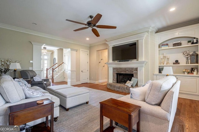 living room with crown molding, ceiling fan, built in shelves, a fireplace, and wood-type flooring