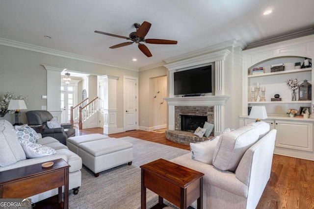 living room featuring a brick fireplace, hardwood / wood-style flooring, ceiling fan, built in shelves, and ornamental molding