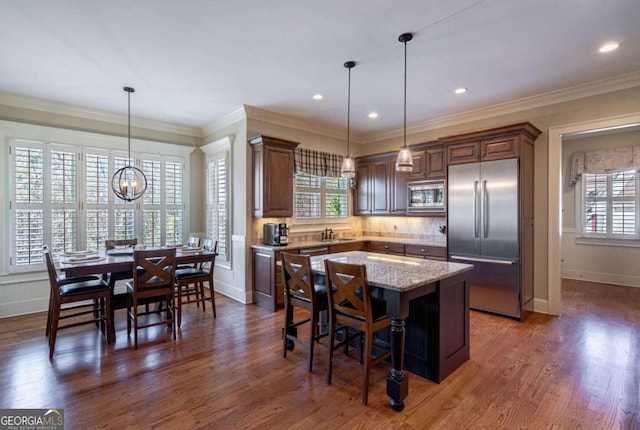 kitchen featuring a center island, dark hardwood / wood-style flooring, built in appliances, crown molding, and pendant lighting