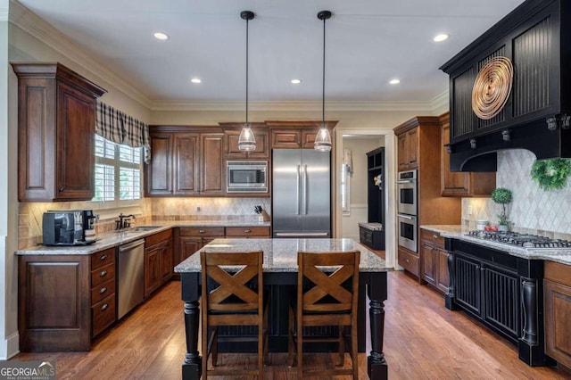 kitchen with light stone countertops, stainless steel appliances, decorative light fixtures, a kitchen island, and light wood-type flooring