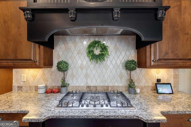 kitchen featuring decorative backsplash, light stone countertops, range hood, and stainless steel gas cooktop