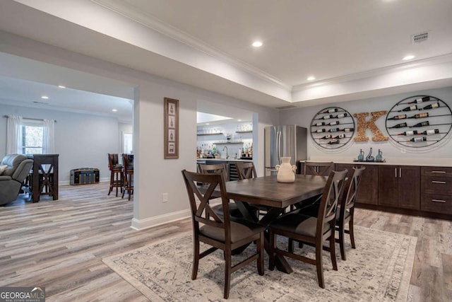 dining space featuring bar, crown molding, and light hardwood / wood-style floors