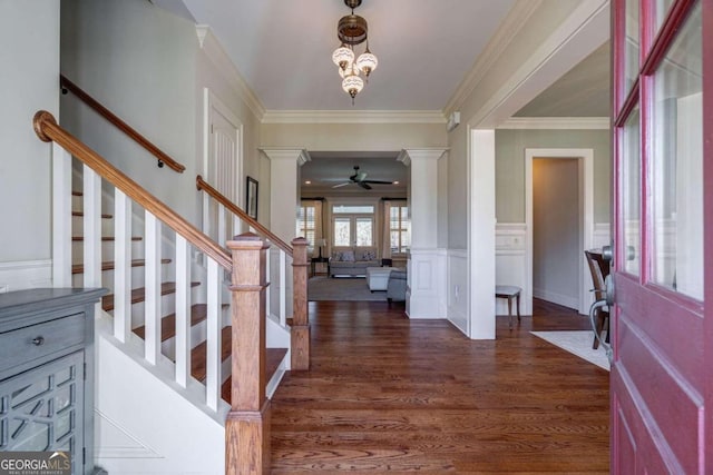 foyer featuring ceiling fan with notable chandelier, ornamental molding, dark wood-type flooring, and decorative columns