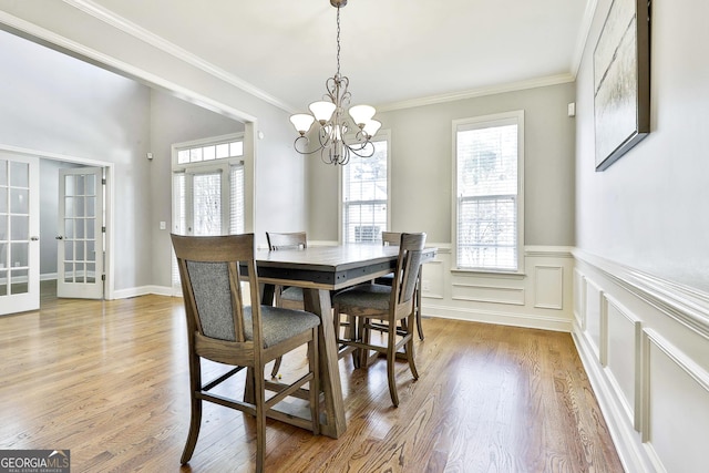 dining space with light hardwood / wood-style floors, ornamental molding, french doors, and a chandelier