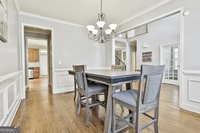 dining space featuring light wood-type flooring, ornamental molding, and an inviting chandelier