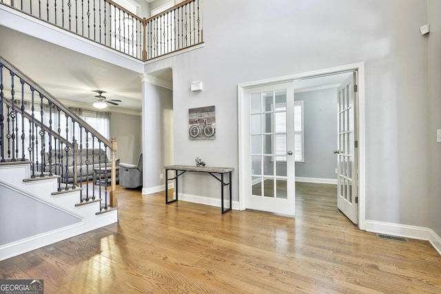 entrance foyer with ceiling fan, french doors, crown molding, a towering ceiling, and wood-type flooring