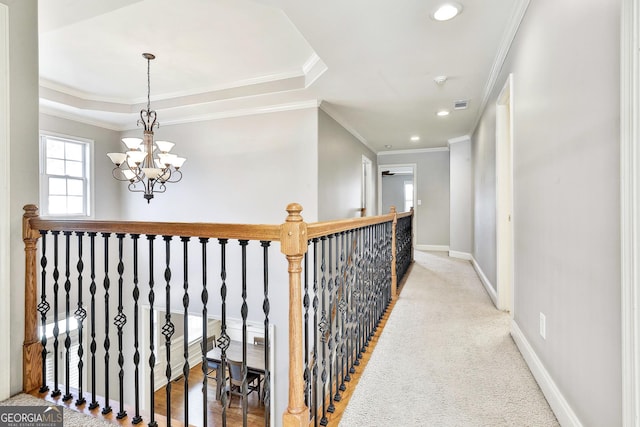 corridor with light colored carpet, an inviting chandelier, a tray ceiling, and ornamental molding