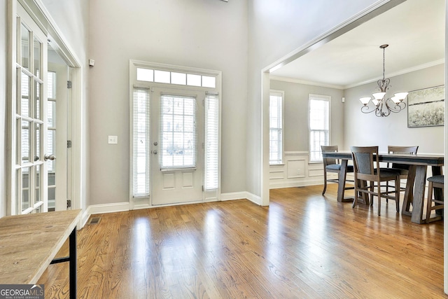 foyer entrance with crown molding, light hardwood / wood-style flooring, a wealth of natural light, and an inviting chandelier