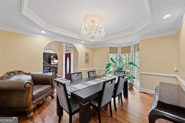 dining space with a tray ceiling, a chandelier, ornamental molding, and hardwood / wood-style flooring