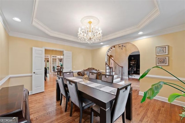 dining room featuring light hardwood / wood-style floors, a tray ceiling, crown molding, and a notable chandelier