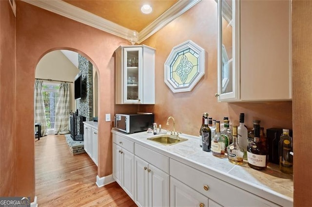 bar featuring white cabinets, light hardwood / wood-style floors, ornamental molding, and sink