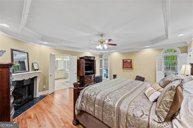 bedroom with ceiling fan, a raised ceiling, ensuite bathroom, wood-type flooring, and ornamental molding