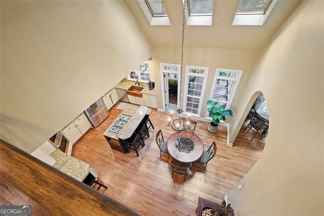 living room with a high ceiling, a skylight, and light hardwood / wood-style flooring