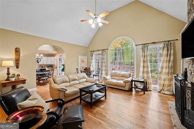 living room with a fireplace, light hardwood / wood-style flooring, high vaulted ceiling, and ceiling fan with notable chandelier