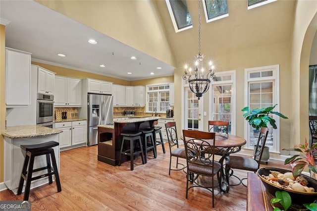 dining area with a skylight, high vaulted ceiling, a chandelier, light wood-type flooring, and ornamental molding