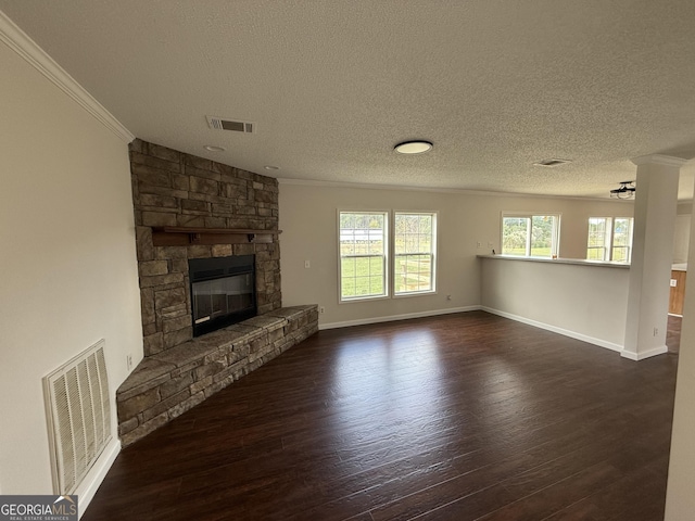 unfurnished living room featuring dark hardwood / wood-style flooring, ornamental molding, a textured ceiling, ceiling fan, and a stone fireplace