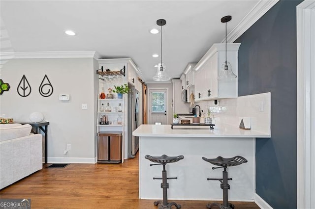 kitchen with white cabinetry, kitchen peninsula, light wood-type flooring, decorative light fixtures, and ornamental molding