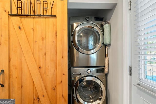 clothes washing area with a barn door and stacked washer / drying machine