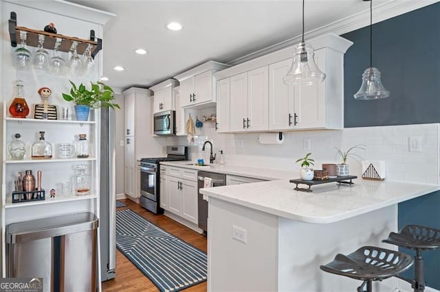 kitchen featuring white cabinetry, hanging light fixtures, stainless steel appliances, kitchen peninsula, and light wood-type flooring