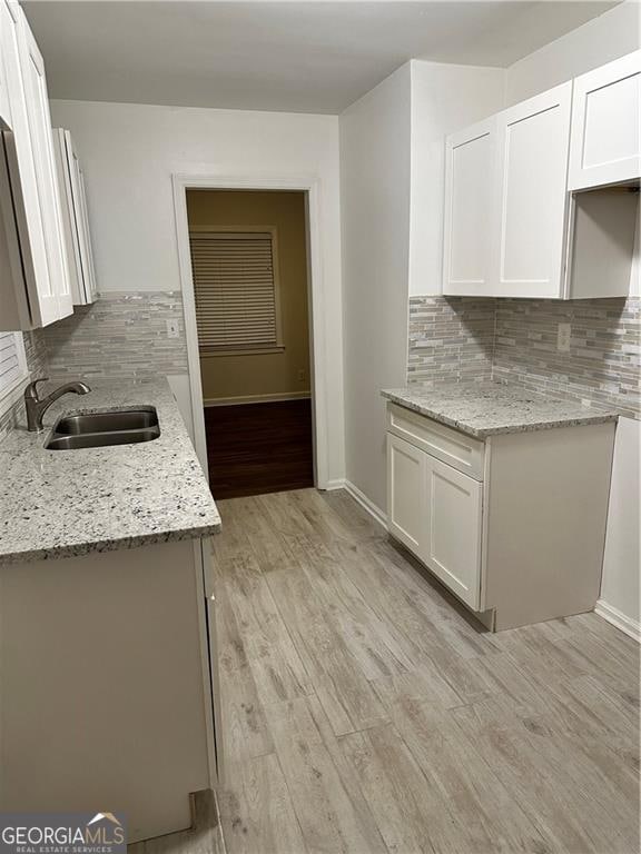 kitchen with sink, decorative backsplash, light hardwood / wood-style floors, light stone counters, and white cabinetry