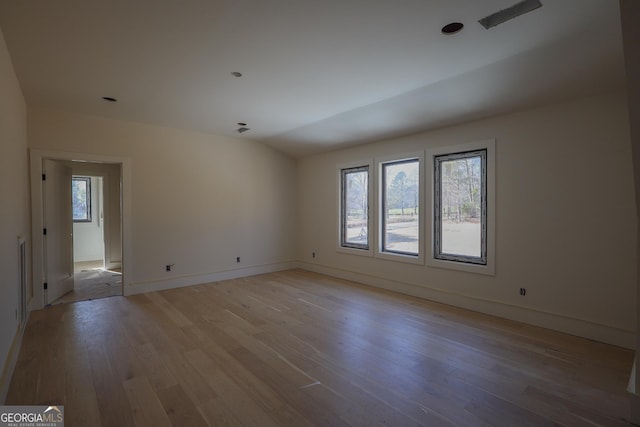 spare room featuring lofted ceiling, light wood-style flooring, and baseboards