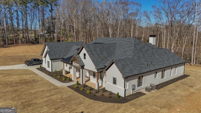 view of front of house featuring central AC, driveway, roof with shingles, a front lawn, and a chimney