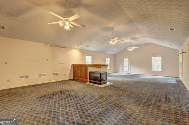 unfurnished living room featuring dark carpet, a textured ceiling, vaulted ceiling, ceiling fan, and a multi sided fireplace