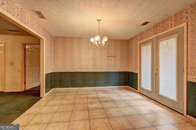 unfurnished dining area with tile patterned flooring, french doors, a textured ceiling, and a notable chandelier