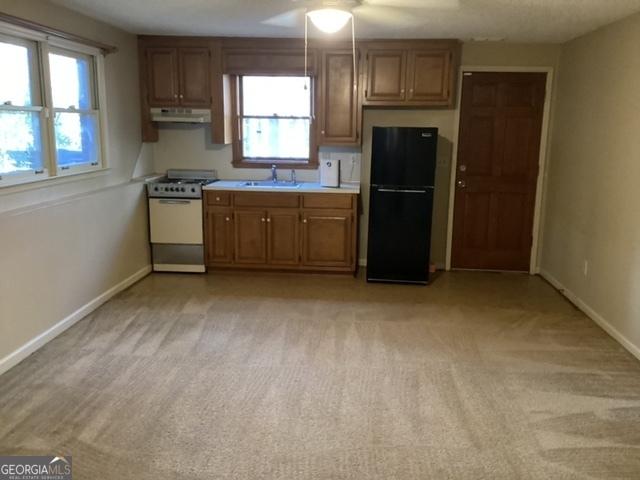 kitchen with stove, light colored carpet, black fridge, and sink