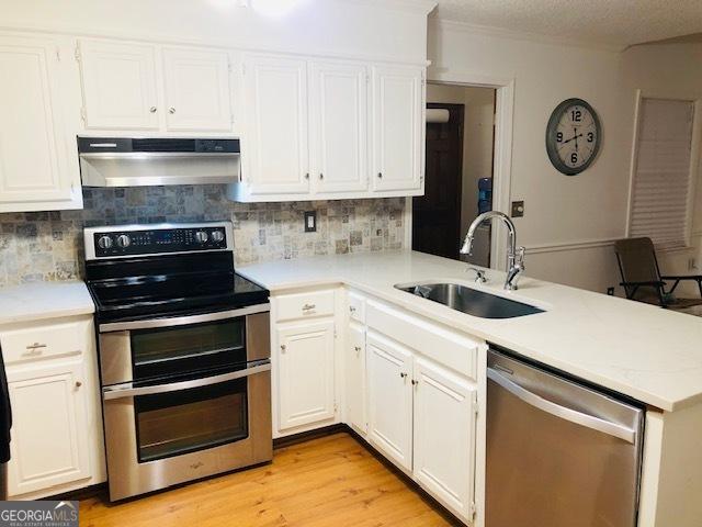 kitchen featuring sink, range hood, kitchen peninsula, white cabinets, and appliances with stainless steel finishes