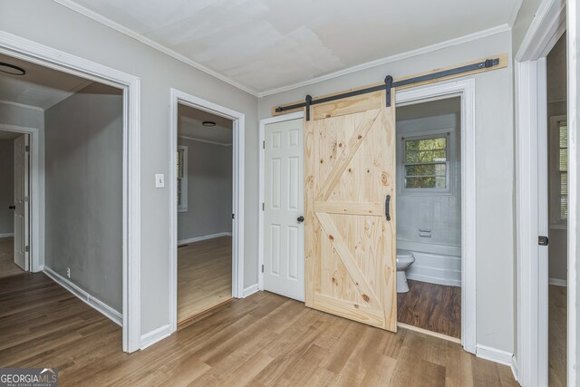 unfurnished bedroom with ensuite bathroom, a barn door, wood-type flooring, and crown molding