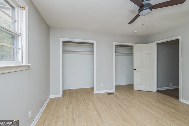 unfurnished bedroom with ceiling fan, light wood-type flooring, and two closets