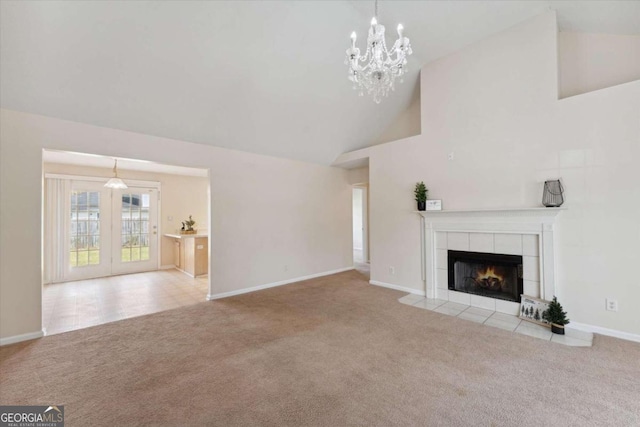 unfurnished living room featuring a tiled fireplace, high vaulted ceiling, light colored carpet, and an inviting chandelier