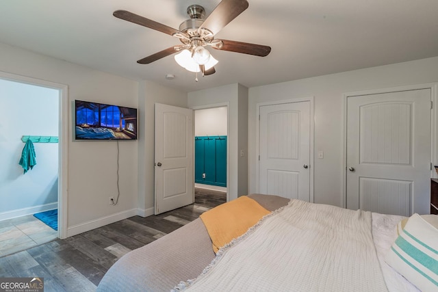 bedroom featuring ensuite bath, dark hardwood / wood-style floors, ceiling fan, and two closets