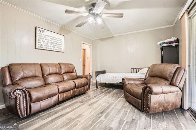 living room featuring ceiling fan, wooden walls, ornamental molding, and light wood-type flooring