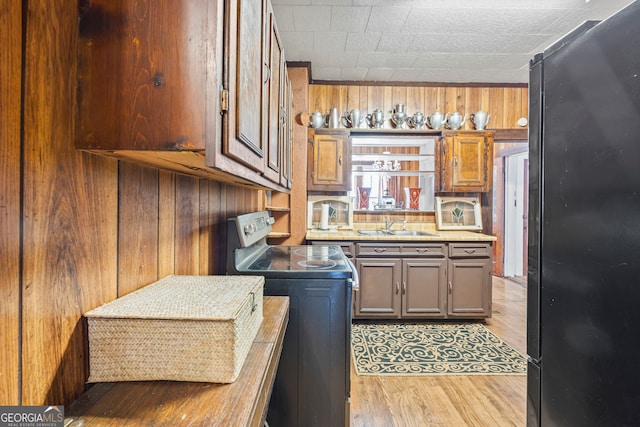 kitchen featuring light hardwood / wood-style floors, stainless steel electric range oven, wood walls, black fridge, and sink