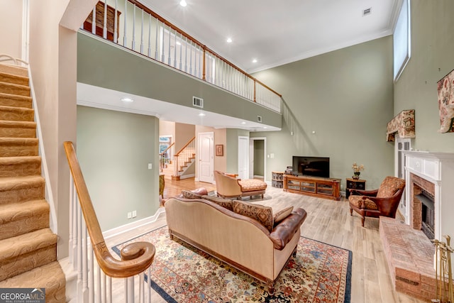 living room with light hardwood / wood-style floors, a towering ceiling, crown molding, and a brick fireplace