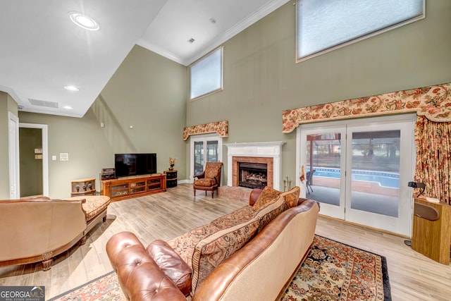 living room featuring a towering ceiling, light wood-type flooring, a wealth of natural light, and ornamental molding