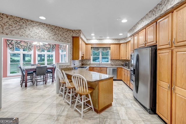 kitchen featuring plenty of natural light, light stone countertops, kitchen peninsula, and stainless steel appliances