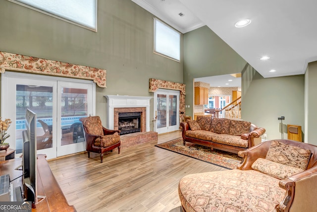 living room with a fireplace, a towering ceiling, light hardwood / wood-style floors, and crown molding