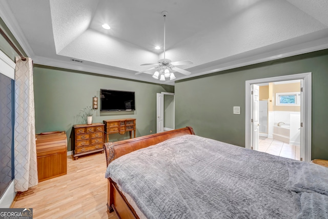 bedroom featuring a textured ceiling, a raised ceiling, ceiling fan, light hardwood / wood-style flooring, and connected bathroom