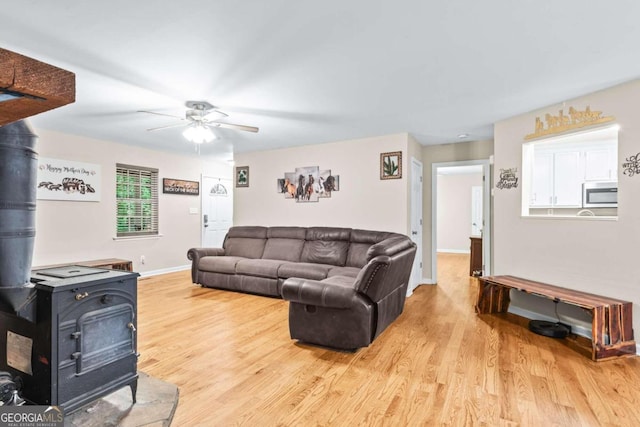 living room with light hardwood / wood-style floors, ceiling fan, and a wood stove